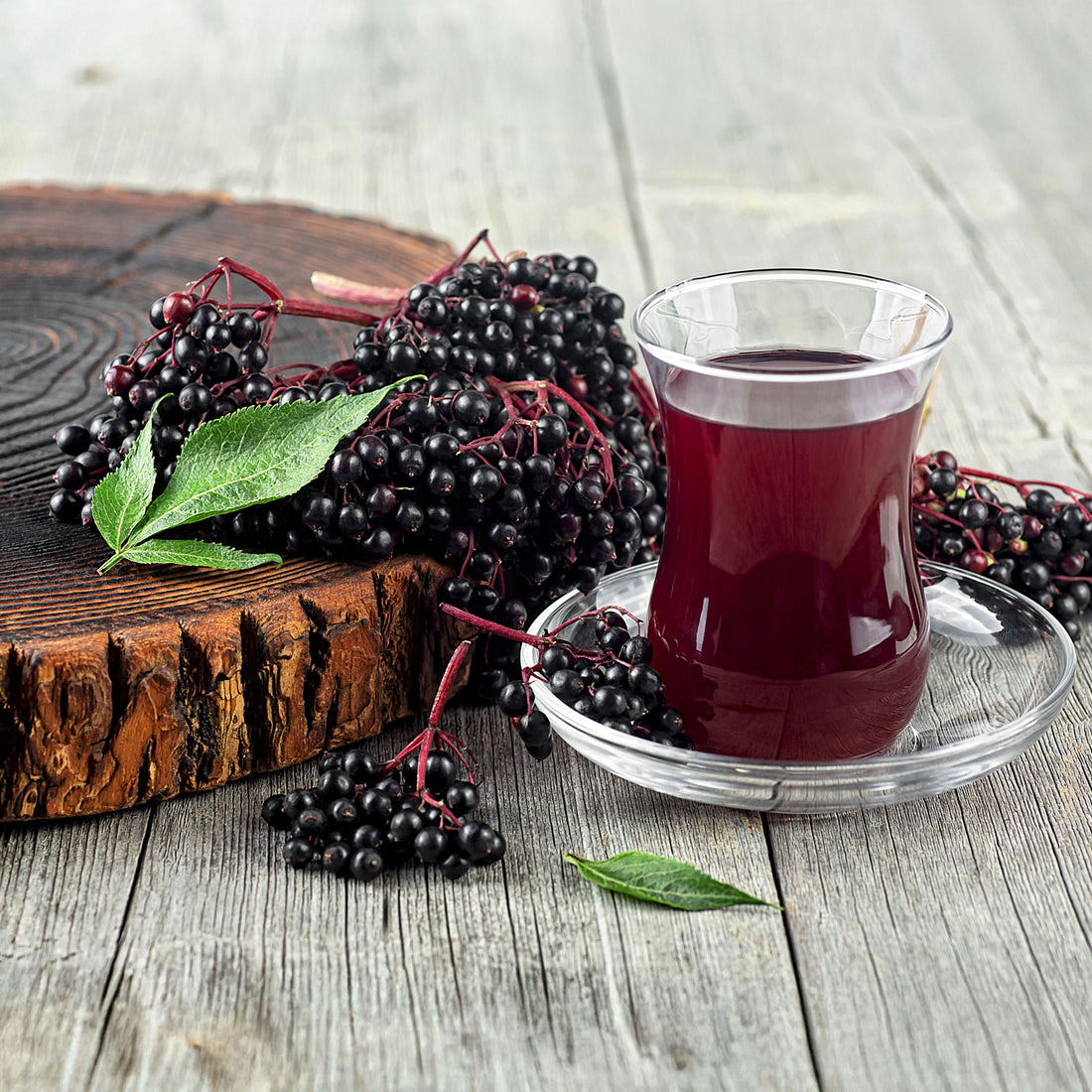 Elderberries on a slice of wood, with a cup of elderberry juice next to them.